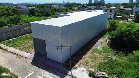 Vista aérea de galpão alongado construído pela Milênio, com fechamento metálico claro e porta de enrolar na fachada, com a cidade ao fundo.