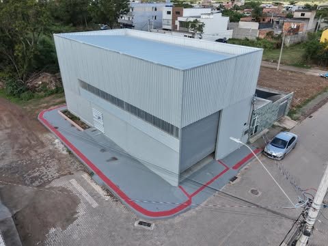 Vista aérea de galpão de esquina construído pela Milênio, com fechamento metálico claro, faixa de ventilação na fachada, porta de enrolar e calçada com contorno vermelho.