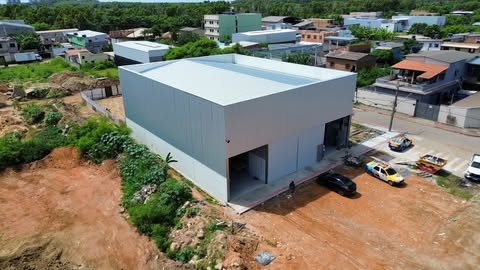 Vista aérea de galpão construído pela Milênio, com fechamento claro e dois acessos amplos na fachada, implantado em terreno com vegetação ao redor.